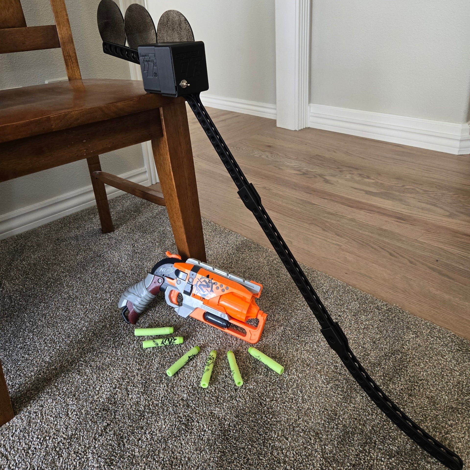 Toy gun with attached hose on a carpeted floor next to a wooden chair.